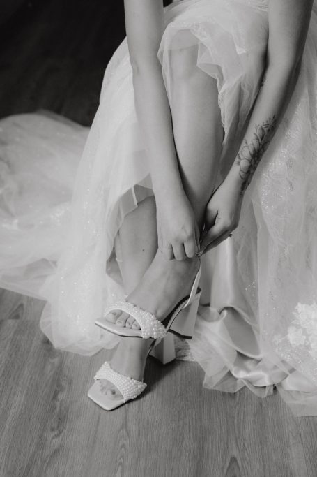 Eine Braut sitzt und zieht sich elegante Schuhe an.