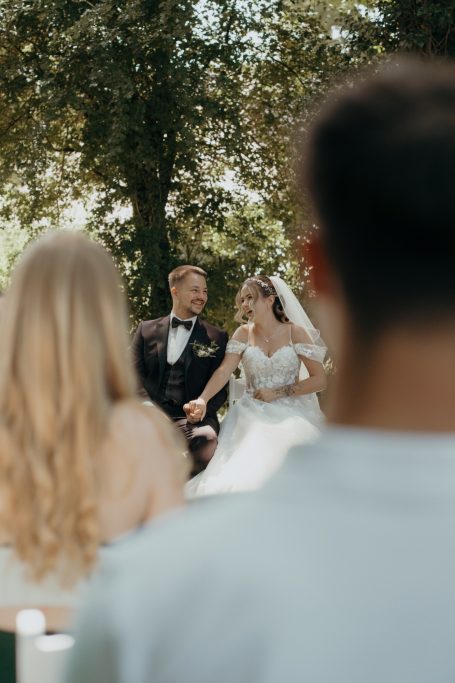 Hochzeitspaar während der Zeremonie unter Bäumen, Blick von den Gästen.