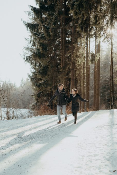 Paar läuft Hand in Hand durch eine verschneite Landschaft mit Bäumen.