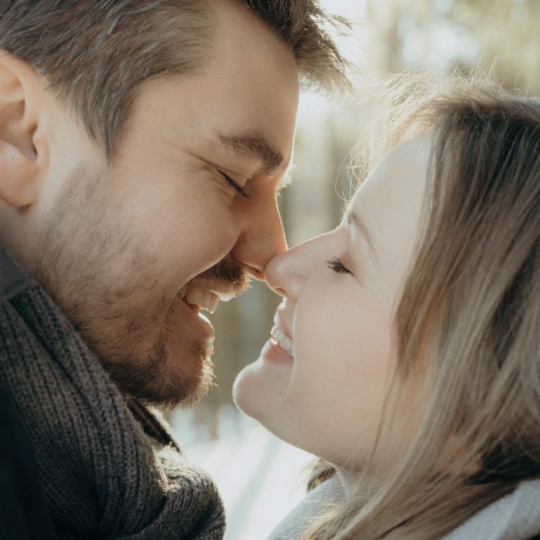 Paar umarmt sich liebevoll, die Köpfe nahe beieinander, in einer natürlichen Umgebung.