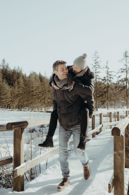 Junger Mann trägt eine Frau auf dem Rücken, während sie durch den Schnee gehen.